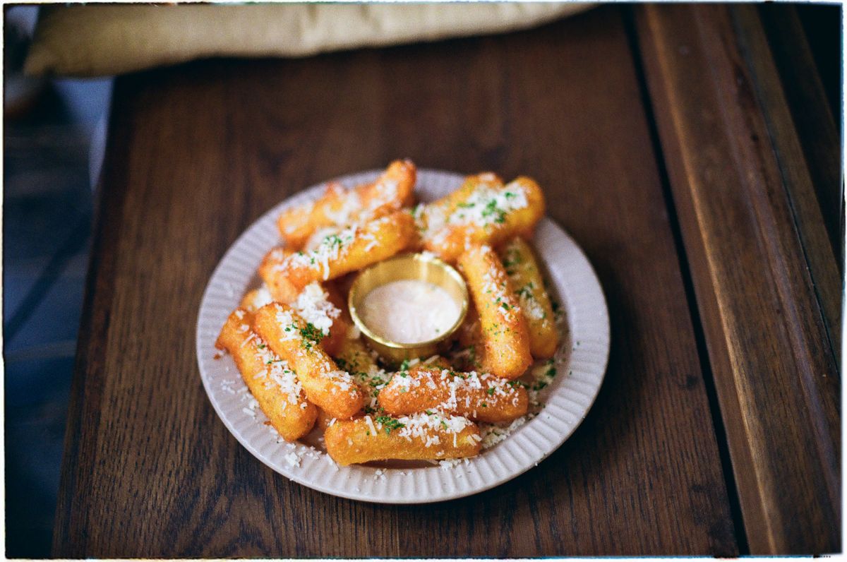 Move Over, Potato Fries: These Crispy Polenta Sticks Bring the Crunch and the Cheese 2 Plate of crispy fried cheese sticks garnished with herbs and cheese, served with dipping sauce.