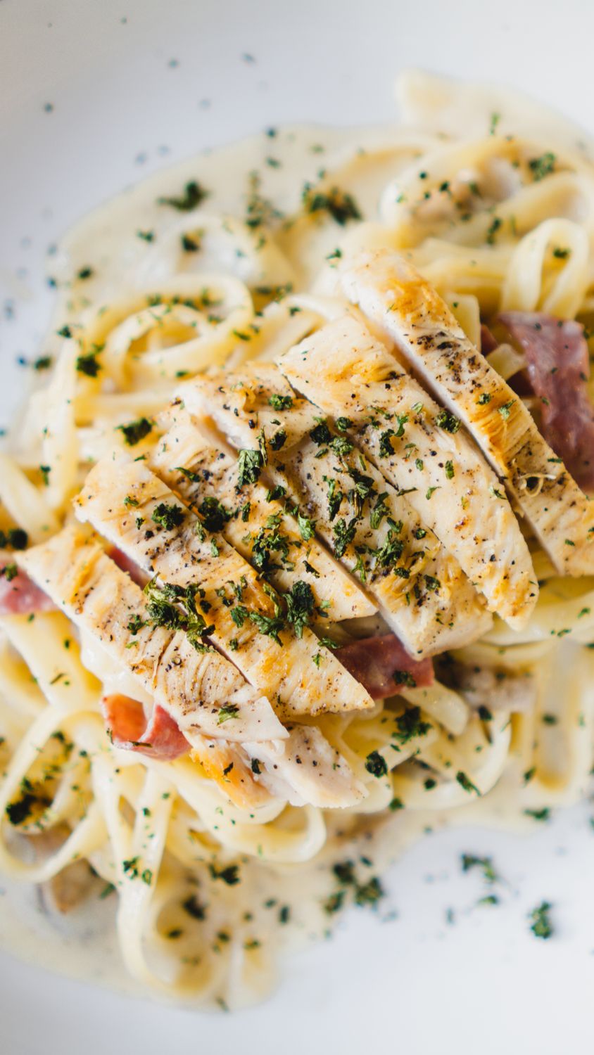 Savor a close-up of creamy chicken fettuccine pasta garnished with parsley, perfect for lunch or dinner.