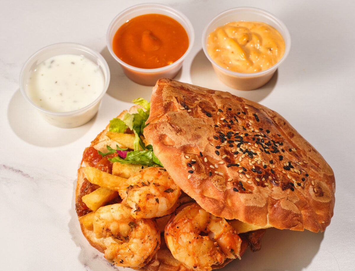 Savor a mouthwatering shrimp po boy sandwich with crispy fries and assorted sauces on a marble surface.