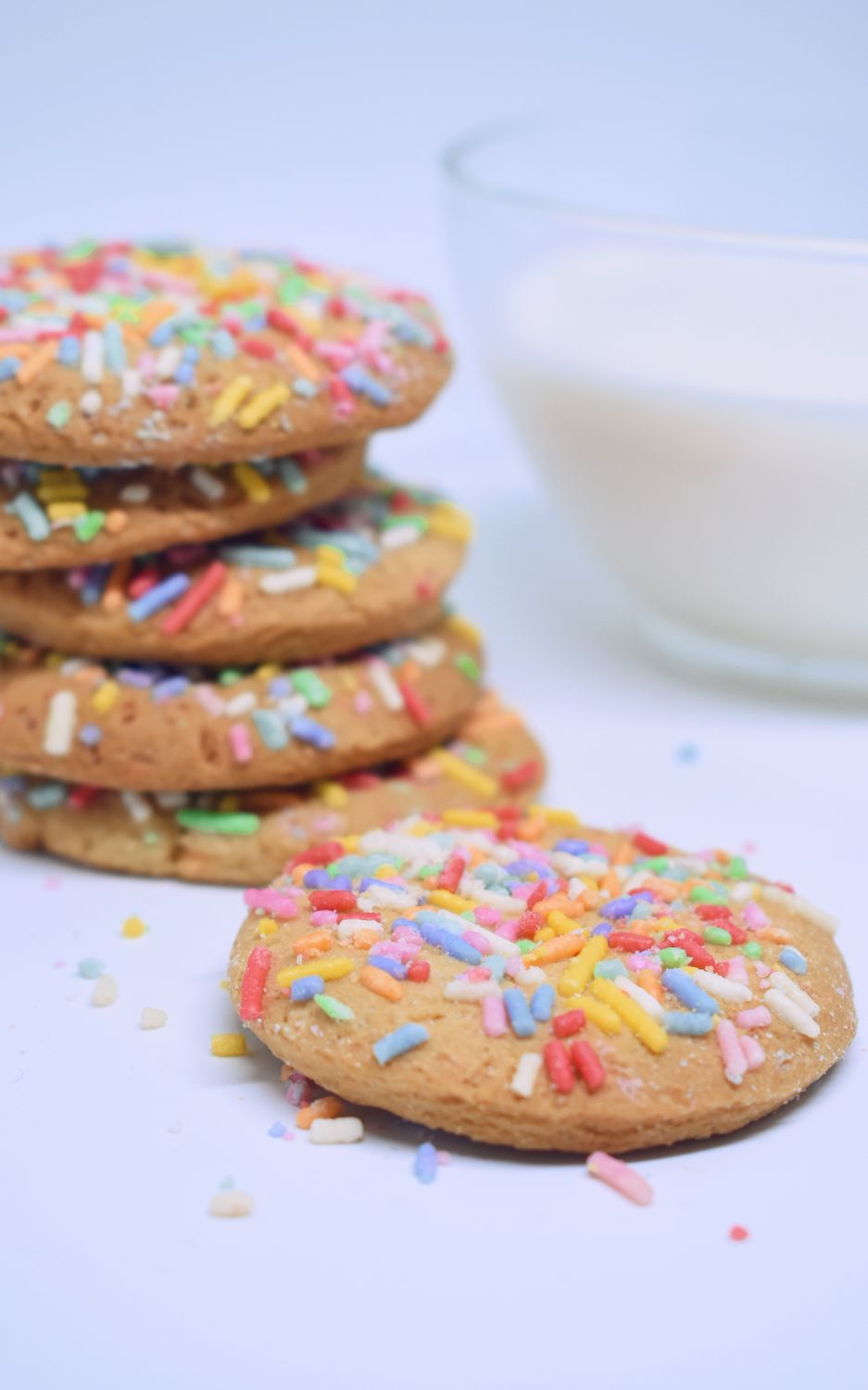 Stack of rainbow sprinkle cookies with milk for a delightful snack.