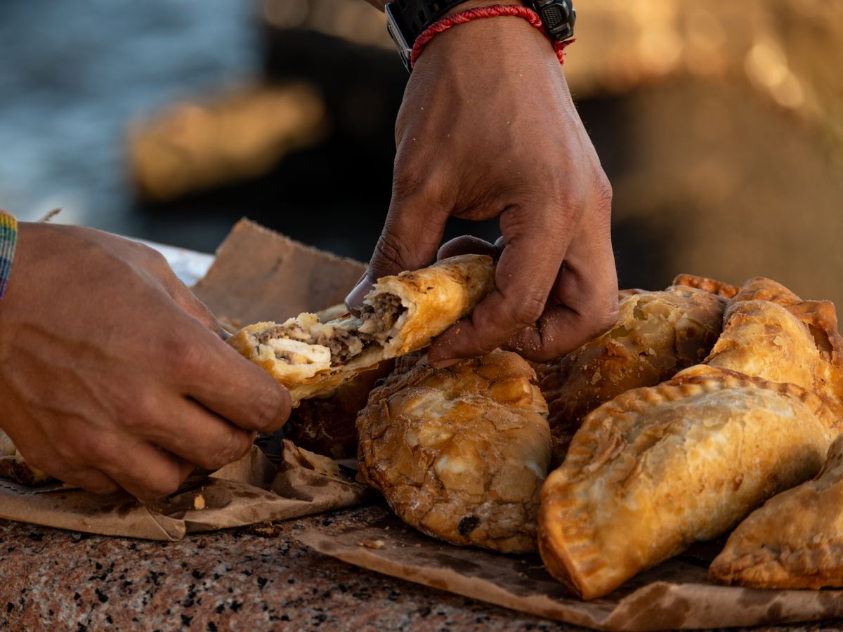 Street food experience with hands opening a crispy empanada in Montevideo, Uruguay.