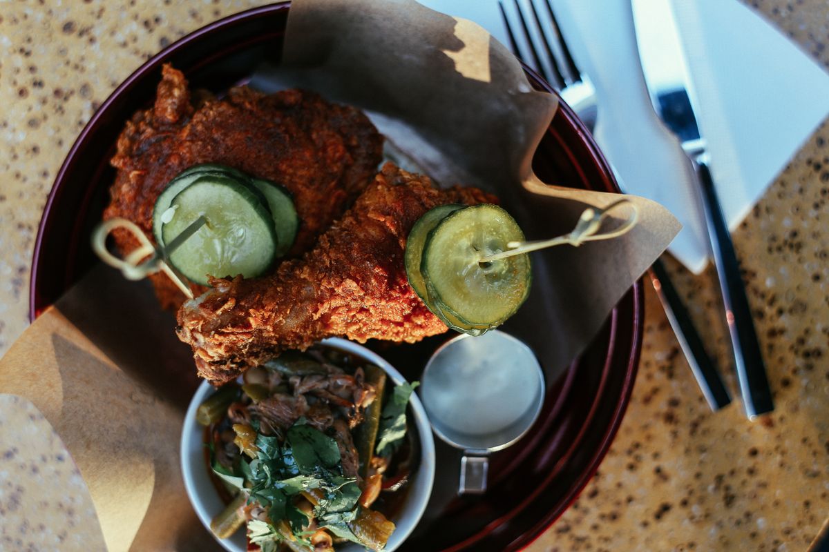 Tantalizing close-up of fried chicken topped with pickles served with a fresh side salad and dressing.