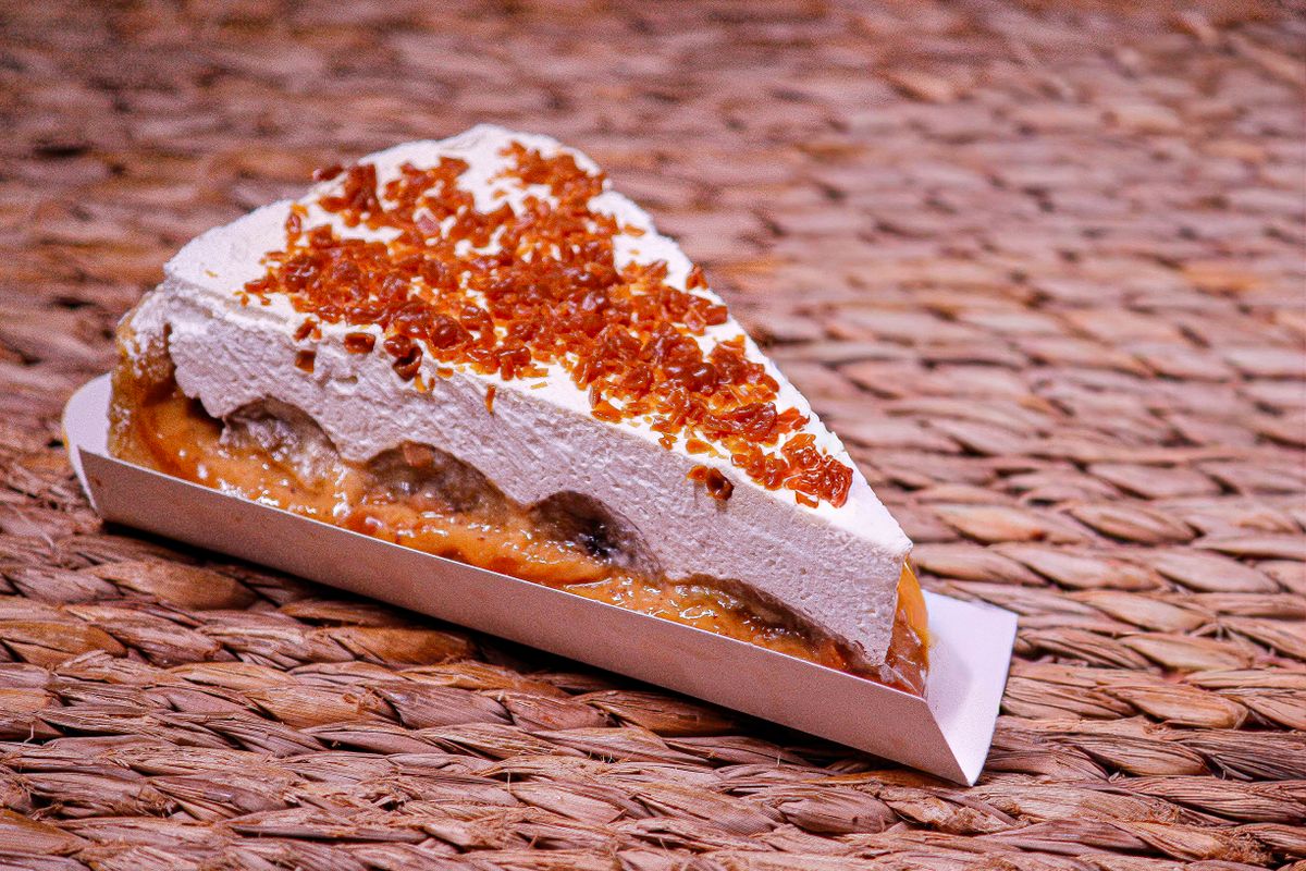 Tantalizing slice of banoffee pie topped with cream and caramel, set on a wicker mat.