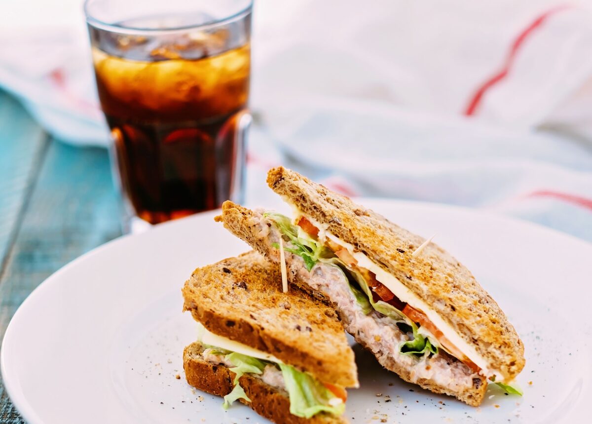 Tasty tuna sandwich served with fresh vegetables and iced tea on a rustic wooden table, perfect for a healthy lunch.