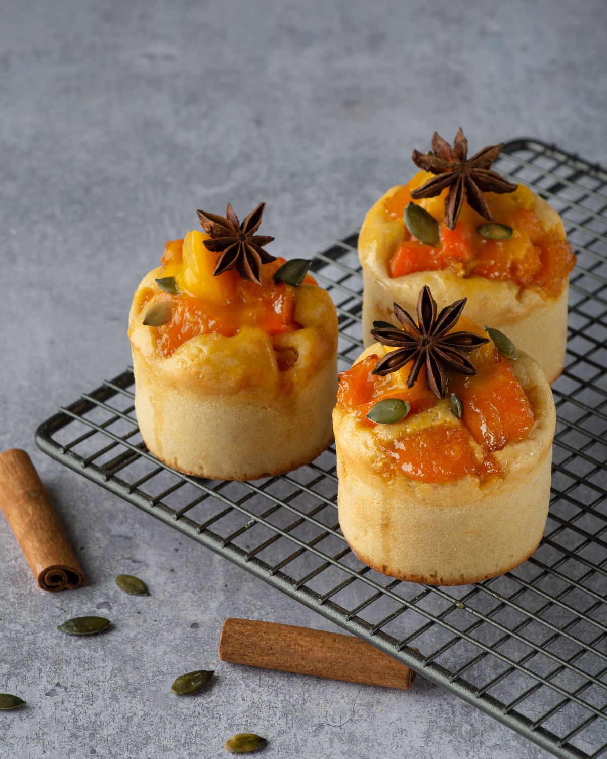 Three delectable pastries topped with cinnamon sticks, star anise, and seeds on a cooling rack.