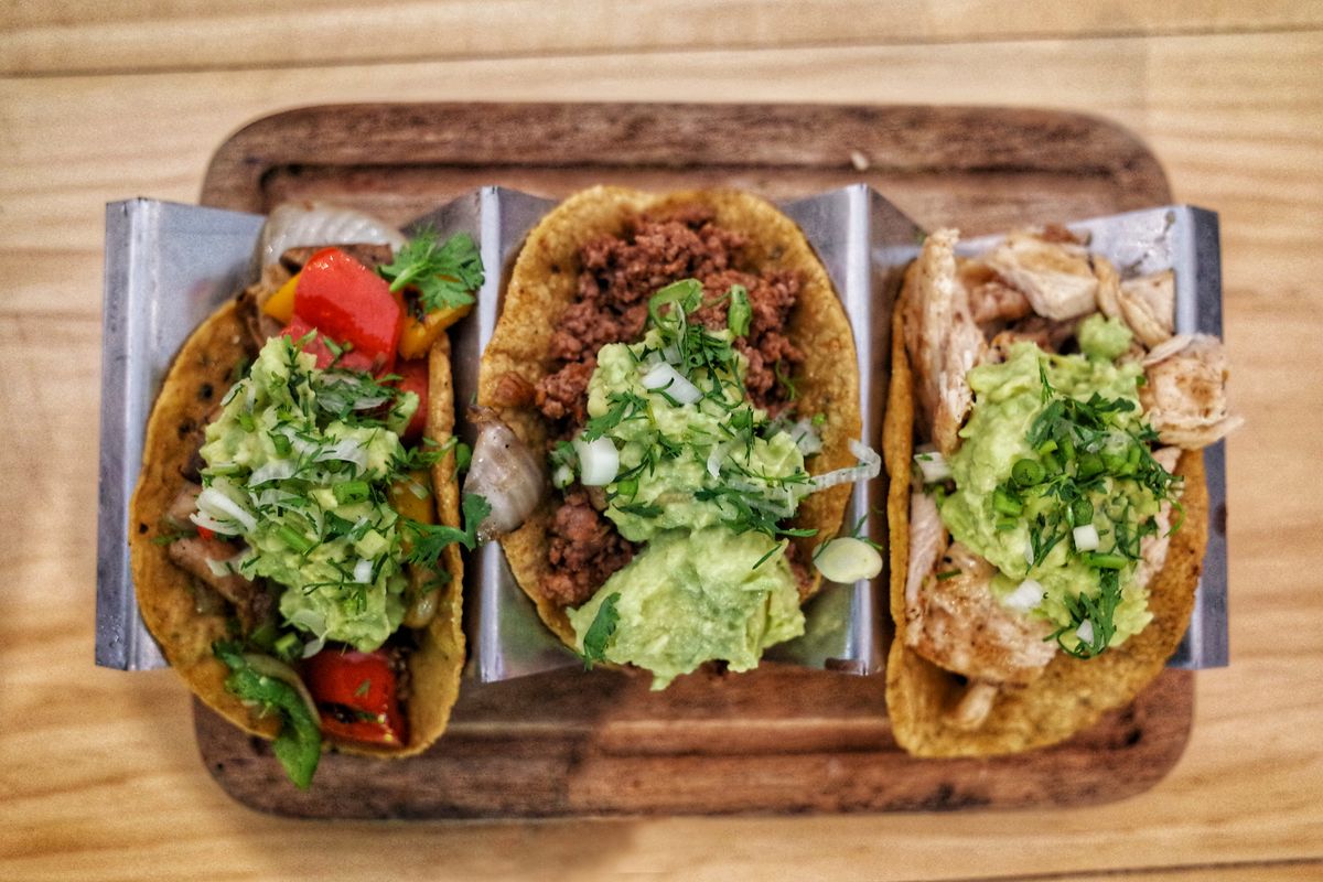 Skip the Menu Overload: 5 Taco Bell Orders That Deserve a Spot in Your Bag 1 Three vibrant tacos with fresh guacamole, veggies, and meat on a wooden tray.