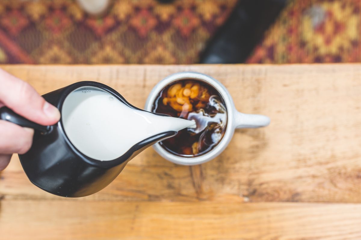Top-down view of milk being poured into a hot cup of coffee on a wooden table.