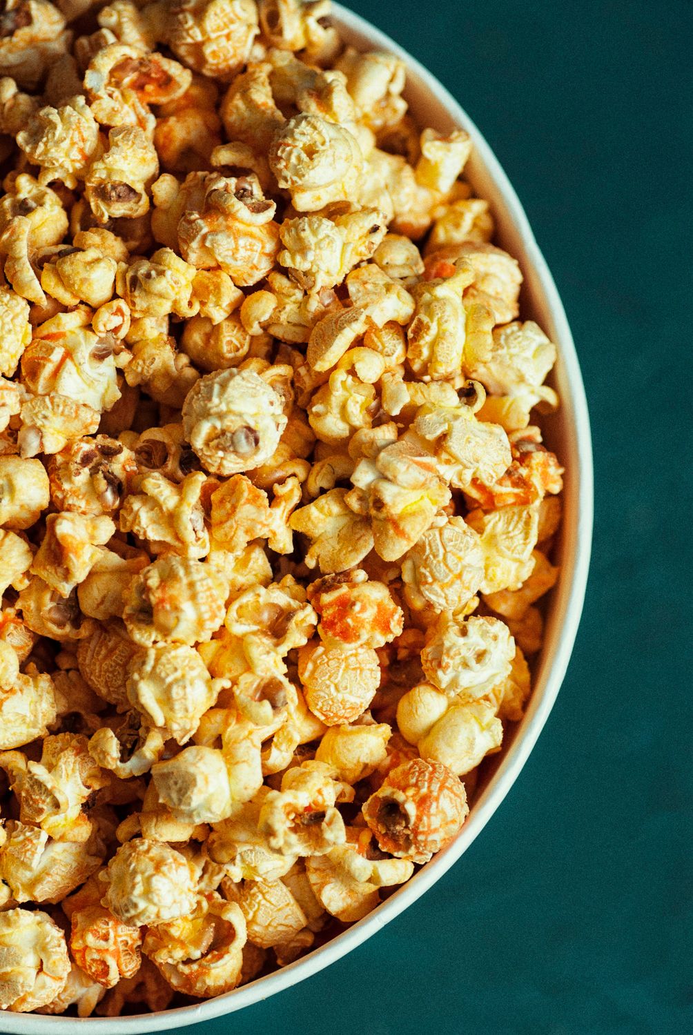 Top view of buttery gourmet popcorn in a white bowl on green background.