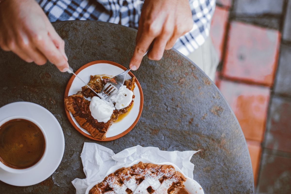 Top view of hands serving a delicious pie with black coffee at a rustic table.