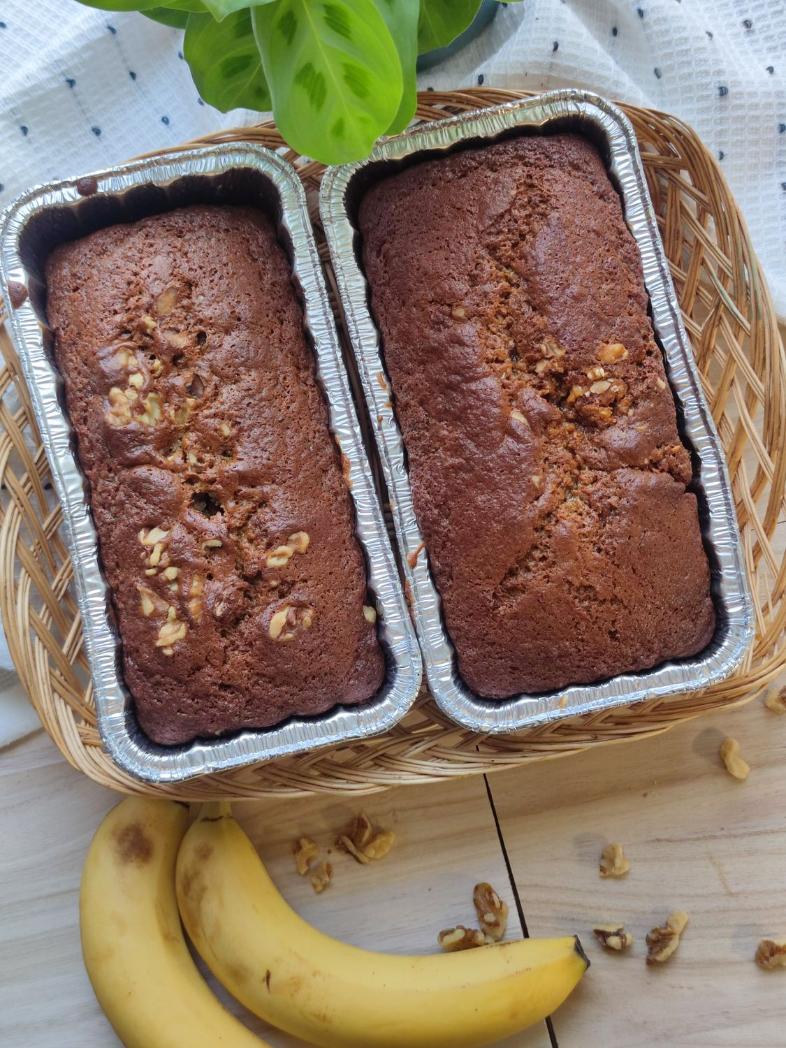 Two freshly baked banana bread loaves with walnuts on a wooden table.