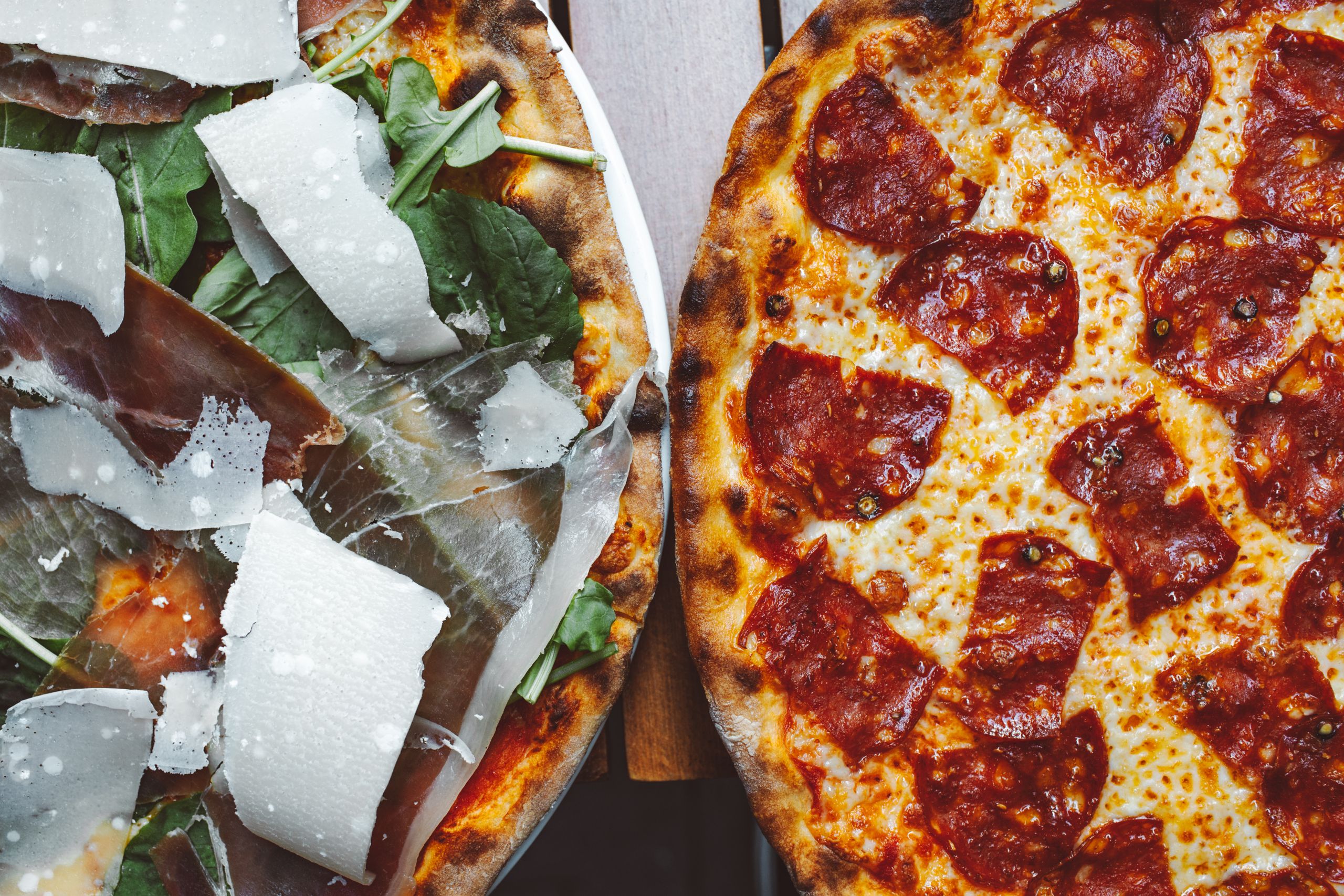 Two gourmet pizzas with mouth-watering toppings including pepperoni and prosciutto, perfect for food photography.