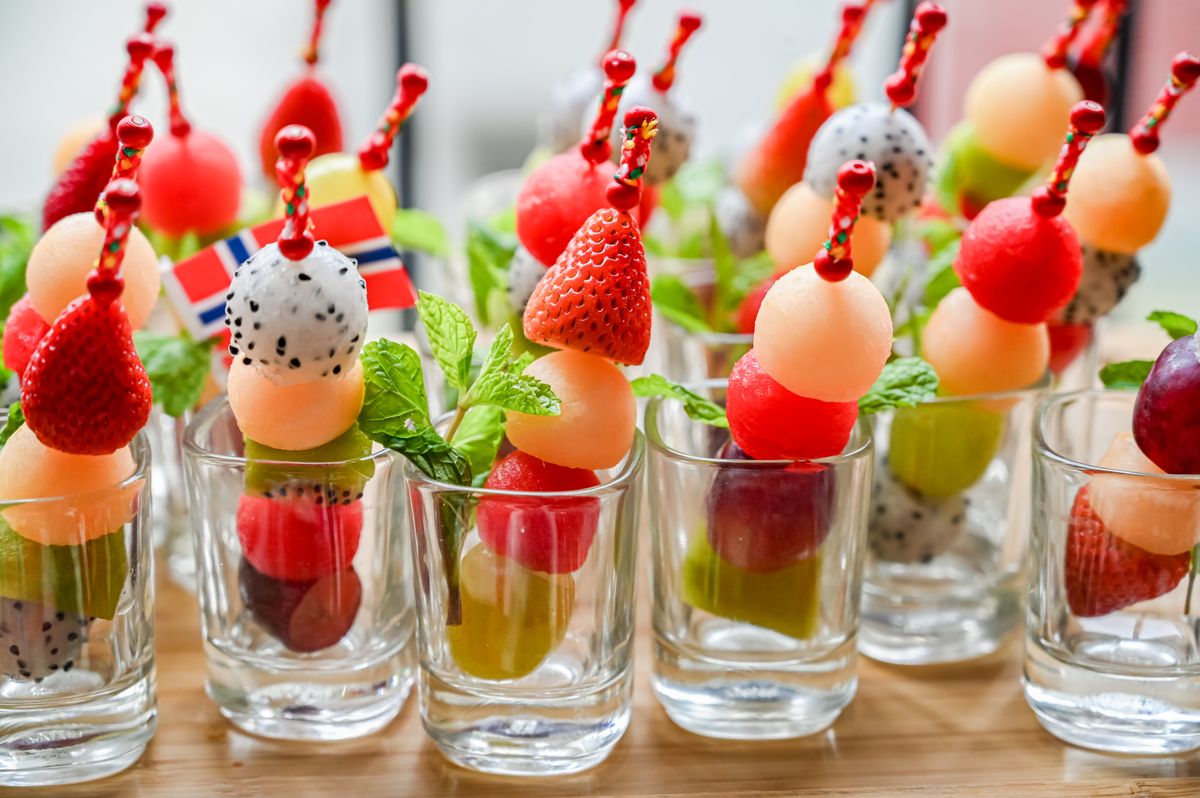 Vibrant fruit skewers in shot glasses with strawberries, dragon fruit, and mint leaves.