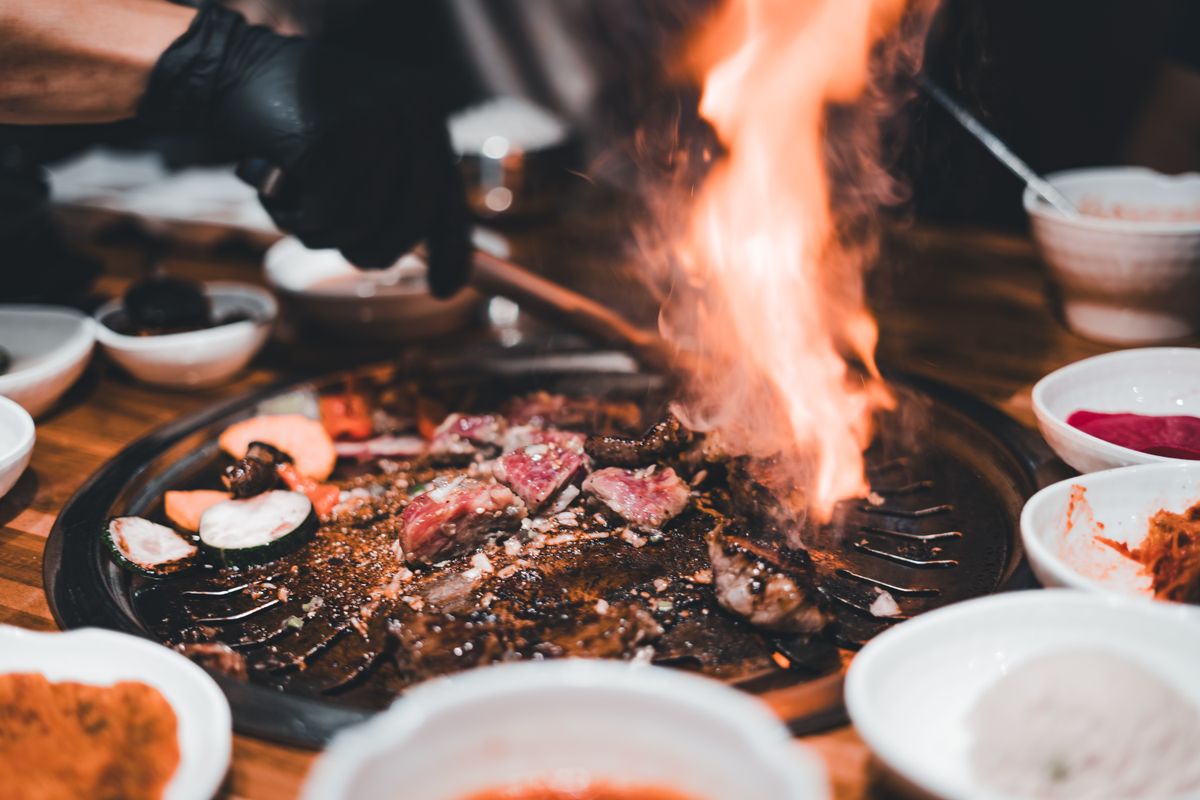 Vibrant Korean BBQ scene showcasing sizzling meats and flames on a grill.