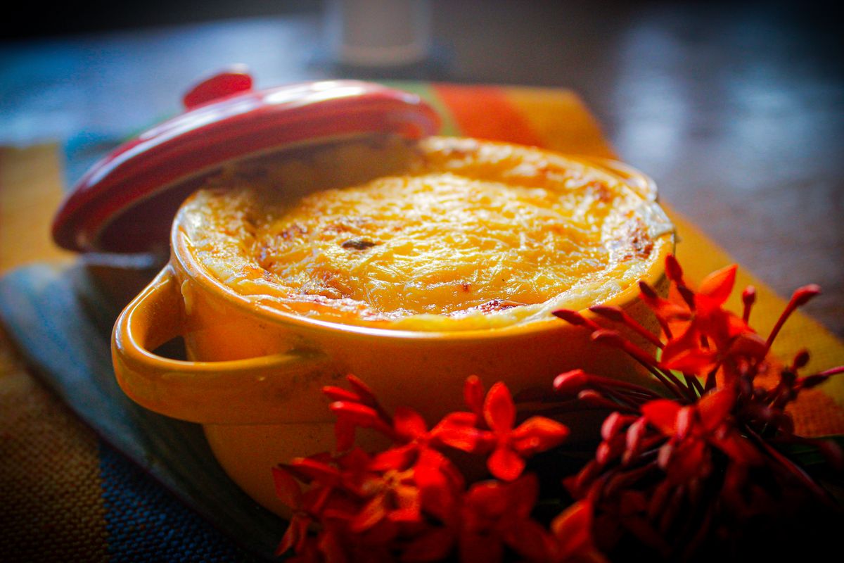 Warm baked dish in a yellow pot with vibrant red flowers on a colorful cloth.