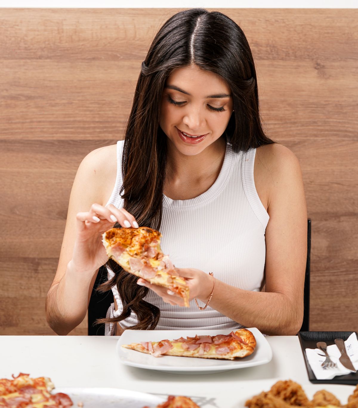 Young woman in a white top enjoying a slice of pizza indoors.