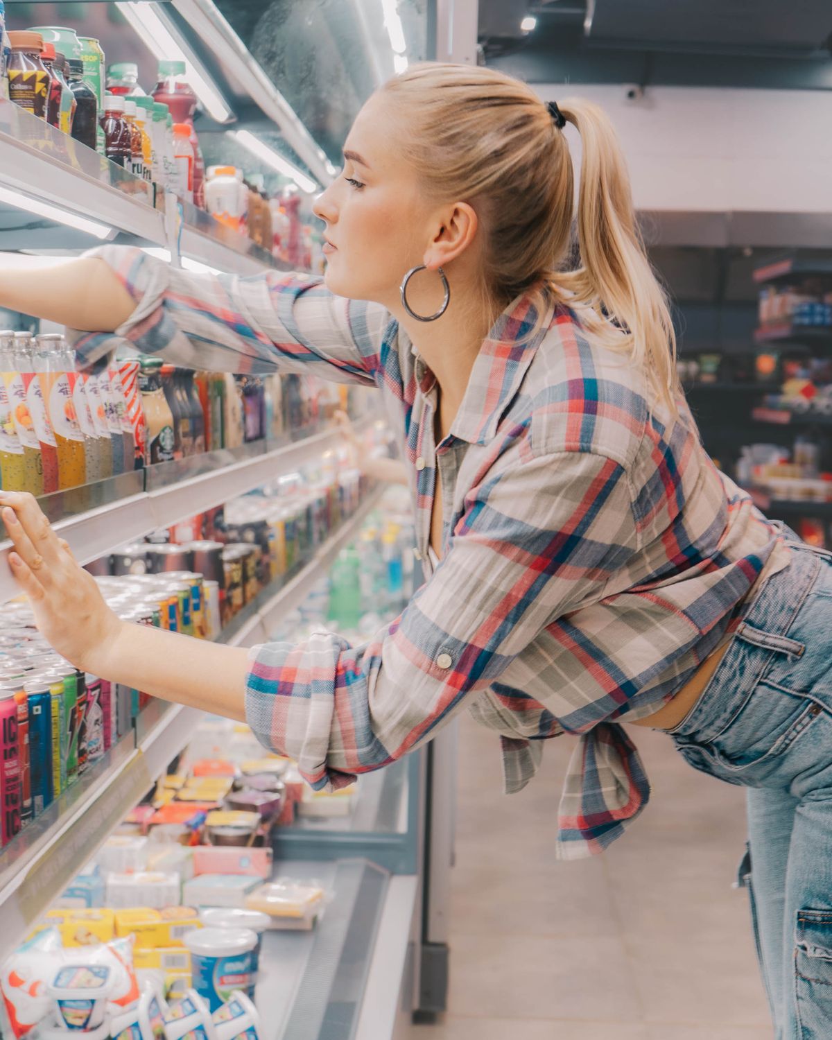 8 Grocery-Store Hot Sauces, Ranked and the Winner Might Start a Fight at Dinner 1 Young woman reaches for a drink on a supermarket shelf. Casual and stylish shopping scene.